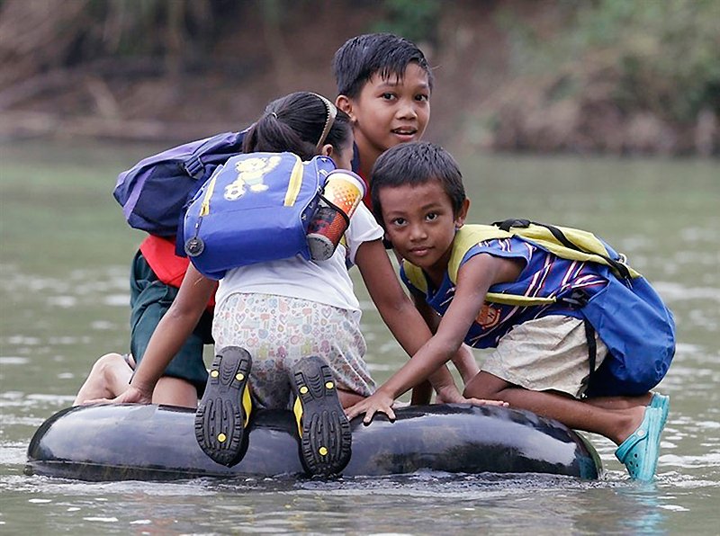 Em área da província de Rizal, crianças cruzam o rio em bóias | Foto: NBC.