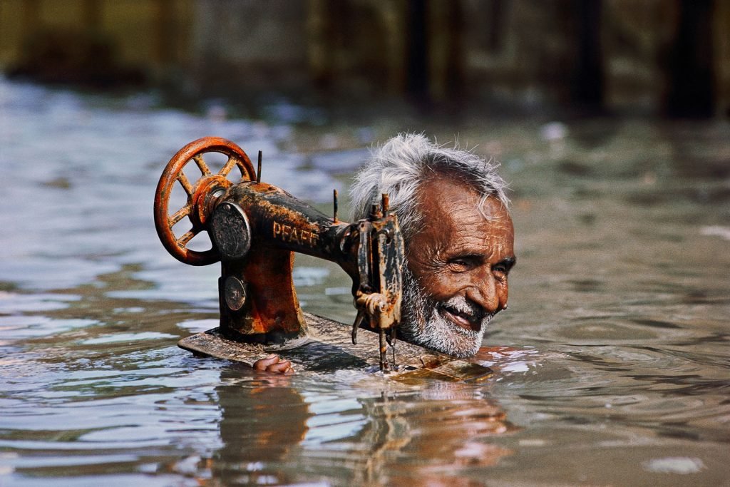 Um alfaiate carrega sua máquina de costura através das águas das monções, Porbandar, Gujarat, 1983